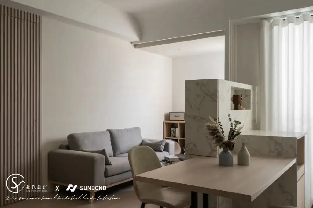 開放式客餐廳設計,以大理石半高隔間牆劃分區域,搭配木質餐桌與灰色布沙發。