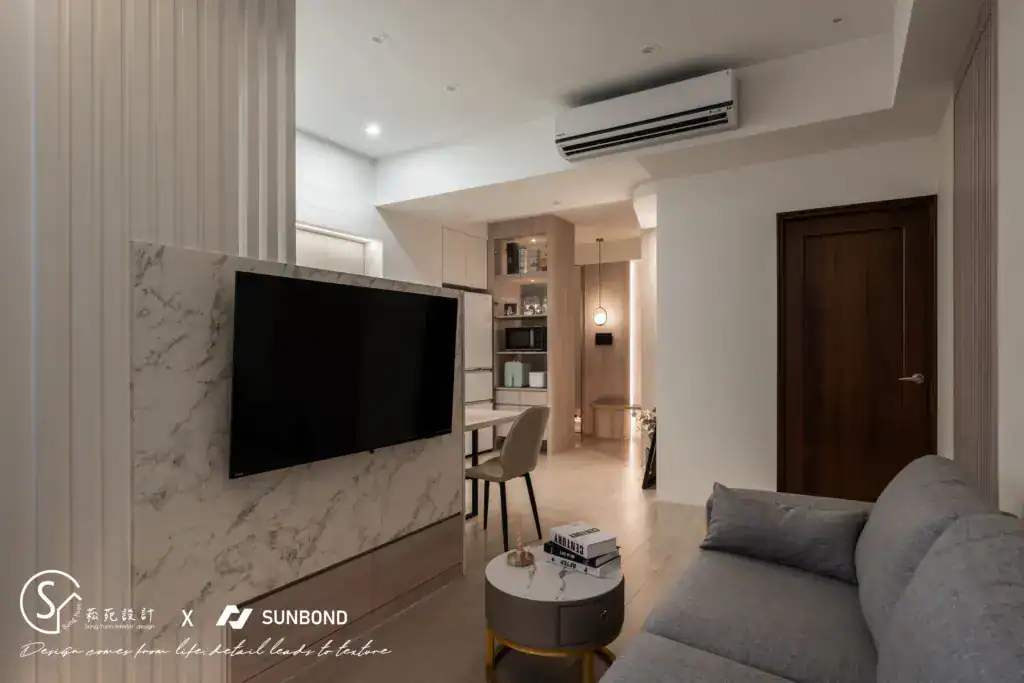 現代公寓客廳,有大理石紋理電視背景牆、灰色沙發、圓形茶幾、分離式冷氣機,背景可見開放式廚房和餐桌。